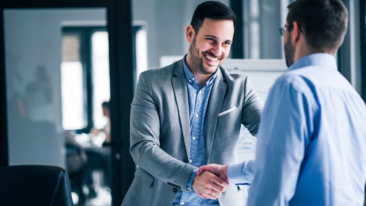 Dois homens em um ambiente de escritório se cumprimentando com um sorriso, simbolizando uma negociação empresarial bem-sucedida por compreenderem o que é trust e aplicá-lo bem