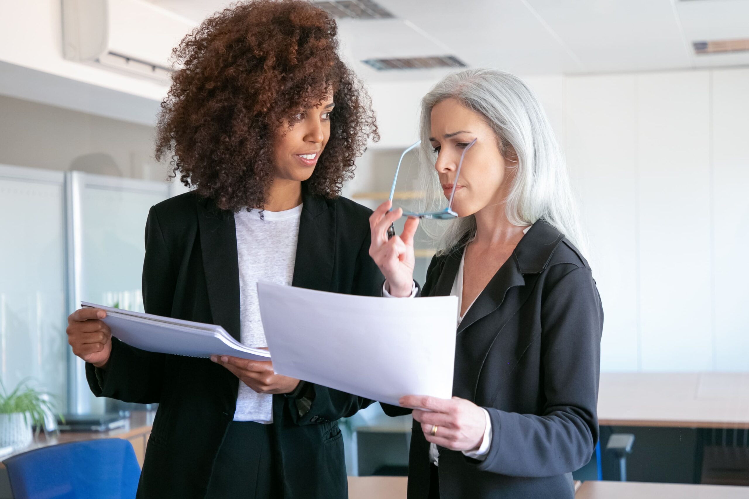 Duas mulheres de negócios discutindo documentos em uma sala de reunião moderna, destacando a importância do trabalho em equipe e comunicação no ambiente corporativo.